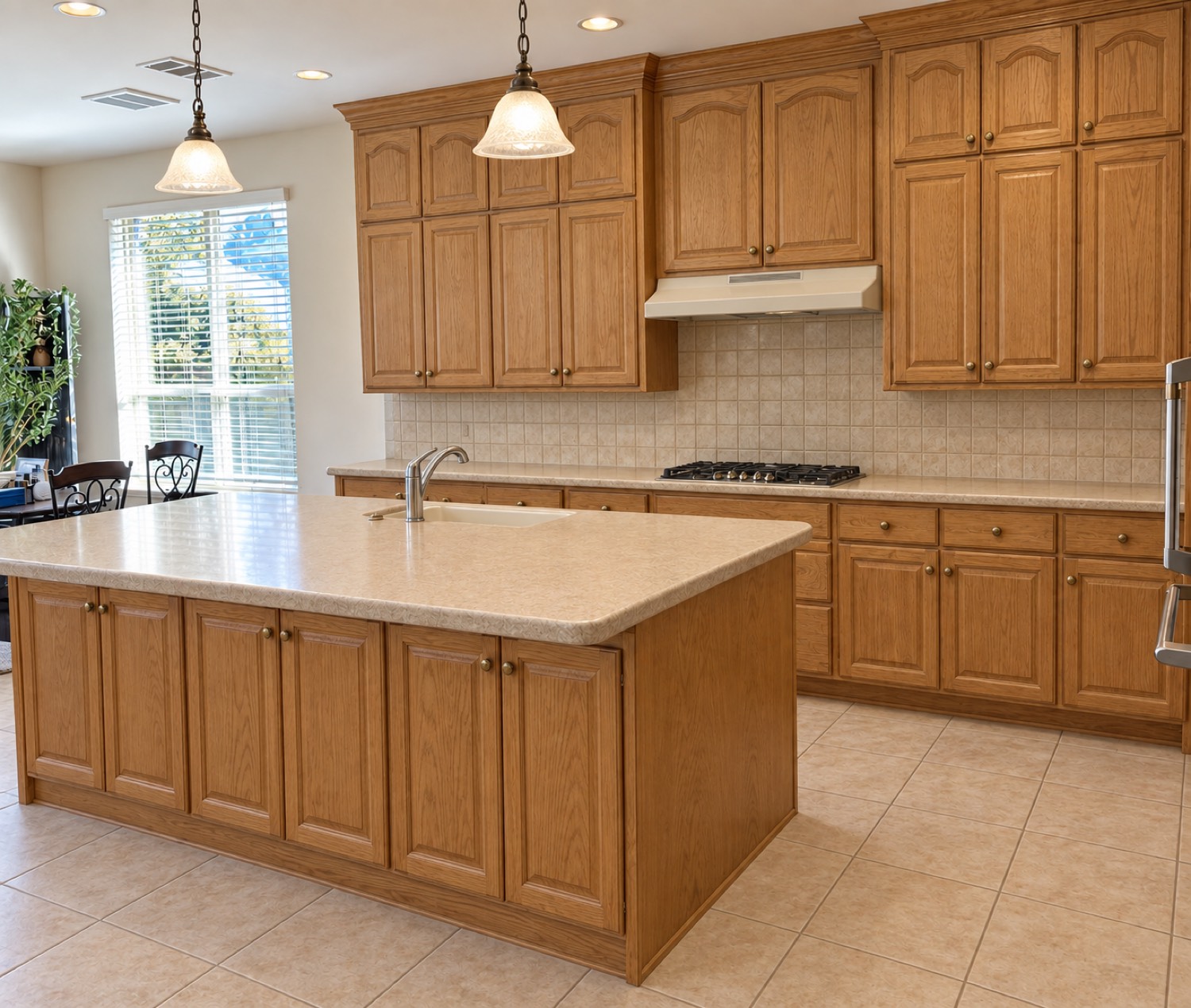 Kitchen before renovation: honey-oak raised-panel cabinets, beige tile backsplash and floor, laminate counters and a recessed range hood