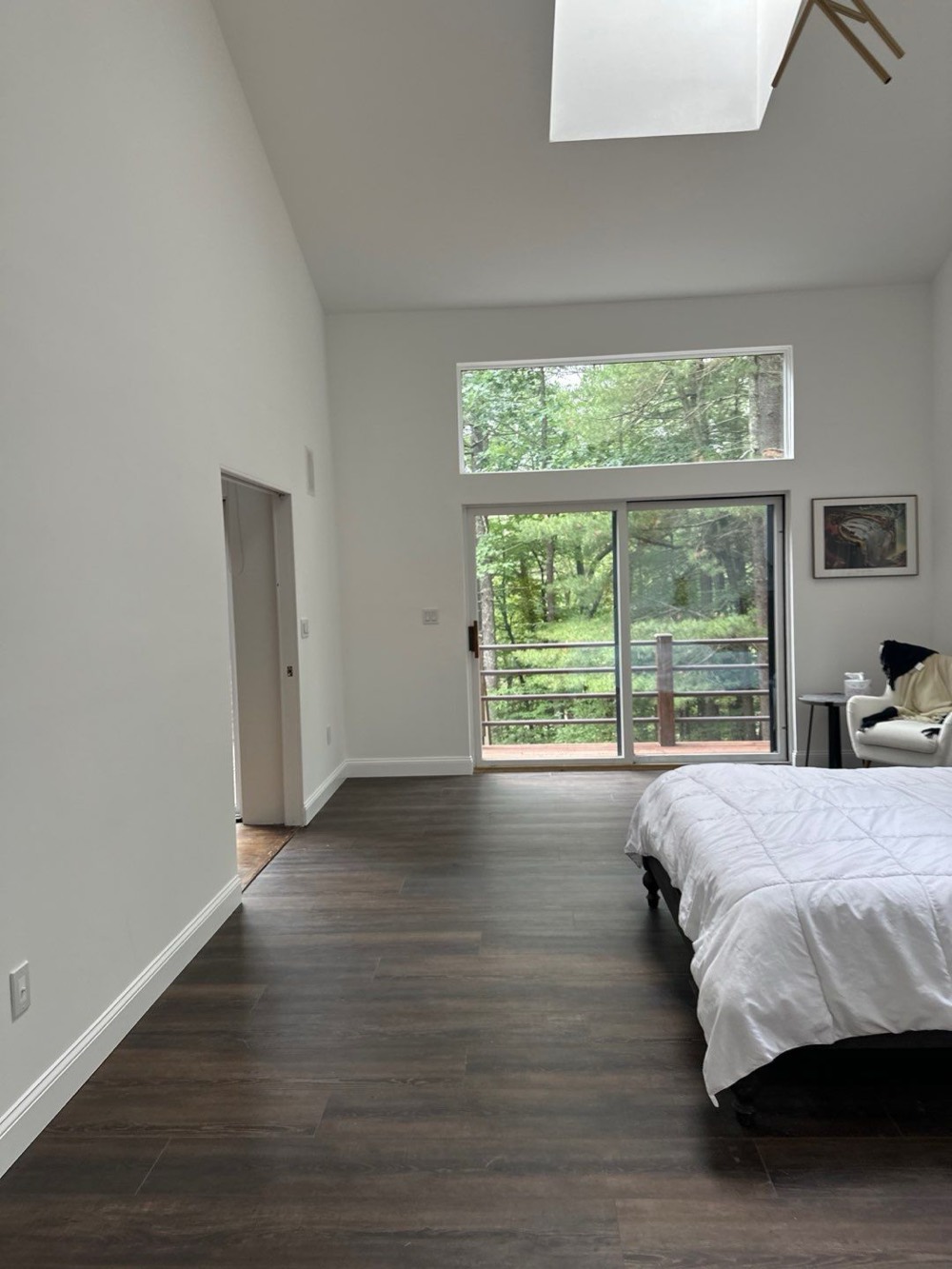 Principal bedroom with a vaulted ceiling, skylight, clerestory window above a sliding glass door to a wooded deck, and wide-plank dark oak floors